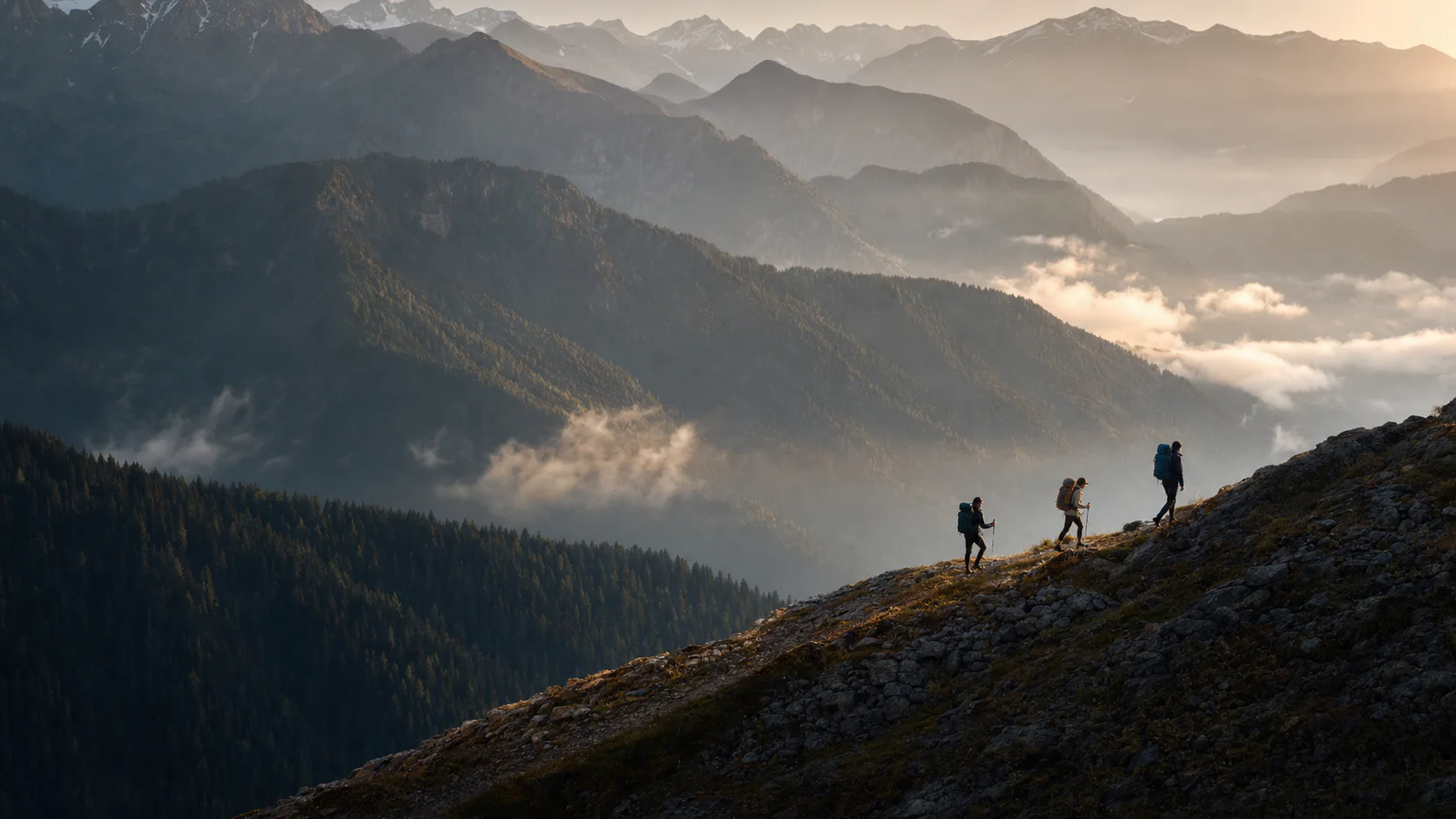 Three hikers crossing a high alpine ridge in the warm light of dawn